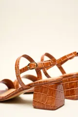 Sandalia de cuero vacuno color negro con textura de cocodrilo, taco cuadrado de 4 cm, punta cuadrada y dos tiras finas, una en el empeine y otra con hebilla en el tobillo.