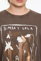 Camiseta de algodón orgánico color negro con efecto gastado, corte oversize y manga corta ancha. Presenta un estampado artístico enmarcado con el texto "BIMBA Y LOLA" en la parte superior e inferior.