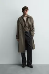 Trench color verde militar, de corte oversized, con cuello con solapas de muesca y manga larga con puño y trabilla. Presenta bolsillos de plastrón con solapa en la cadera y un bolsillo interior. Tiene una abertura en el centro de la espalda y cierre frontal de botonadura cruzada.