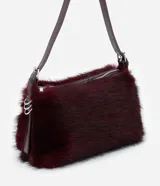 Cartera mediana de pelo sintético color bordó, con asa única de cuero sintético brillante, cierre superior por cremallera y detalles de argollas metálicas en los laterales.