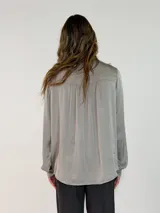 Camisa de satén color naranja óxido, con cuello mao y lazo para anudar. Presenta volados decorativos en el frente y en las mangas, las cuales son largas y terminan en puños abotonados.