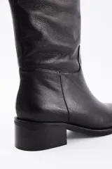 Bota de caña alta confeccionada en cuero vacuno, con taco cuadrado bajo y punta redondeada.