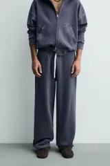Pantalón jogger de corte wide fit confeccionado en algodón con interior de rizo. Presenta cintura elástica ajustable con cordón, bolsillos laterales y un bolsillo trasero de plastrón. Cuenta con un efecto lavado y acabados irregulares en el ruedo.