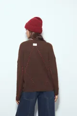 Sweater de tejido suave color marrón con diseño de líneas bordadas en color rojo. Presenta cuello redondo, manga larga y calce relajado.
