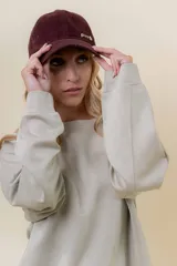 Gorra de diseño clásico con visera curva, confeccionada en material símil gamuza color bordó. Presenta un logo metálico con la palabra Peach en la parte frontal y cuenta con un sistema de ajuste posterior.