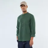 Camisa de manga larga de franela verde oscuro, con cuello mao y cierre frontal de botones marrones. Posee un bolsillo de parche en el pecho izquierdo.