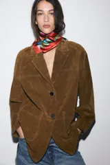Chaqueta larga de piel con cuello solapa, manga larga y cierre frontal con botones. Presenta bolsillos delanteros de plastrón y un diseño estructurado.