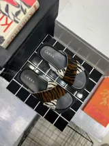 Sandalias chatas con base cuadrada negra y tiras cruzadas de cuero con estampado animal print de cebra y tigre.