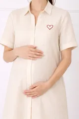 Camisa maternal color beige, de viscosa suave y liviana, con cuello camisero, botones frontales y mangas cortas. Presenta un bordado de corazón rojo en el pecho.