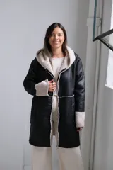 Tapado de cuero sintético negro con interior y detalles en corderito sintético color crema. Presenta capucha, cierre frontal y mangas largas con puños vueltos.