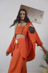 Pollera tipo tubo de lino color naranja, de corte midi, con detalle de hebilla en chapón de bronce en la cintura.