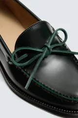 Mocasín de vestir fabricado en piel con acabado brillante, presenta un detalle de lazo en el empeine y suela a contraste con ligero tacón.