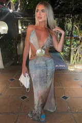 Vestido largo con estampado abstracto en tonos grises, celestes y marrones. Presenta escote halter con abertura en el abdomen unida por un adorno de concha.