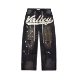 Pantalón de jean negro, corte baggy, con efecto desgastado, salpicaduras de pintura blanca y roturas. Presenta un aplique frontal con la palabra "Valley" bordada con lentejuelas de colores. Tiene cordón de ajuste en la cintura.