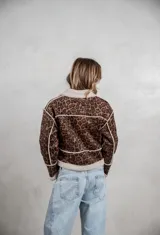 Campera de gamuza con estampado de leopardo en tonos grises, con interior y bordes de corderito sintético color crema. Presenta cierre frontal con botones tipo toggle y diseño de corte recto.