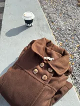 Tapado corto de paño color marrón, con cuello bebé, cierre frontal cruzado con cuatro botones y diseño entallado con costuras verticales.