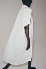 Vestido camisero de lino con cuello solapa, manga corta y cierre frontal con botones. Presenta un diseño con bajo redondeado y aberturas laterales.