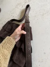 Cartera de hombro confeccionada artesanalmente en cuero gamuzado color marrón, con diseño de múltiples volados horizontales y correa ajustable con hebilla metálica.