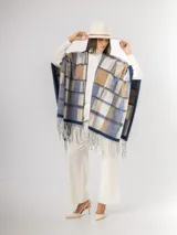 Ruana abierta con diseño de cuadros en tonos azul, beige y blanco, con terminación de flecos en el ruedo.