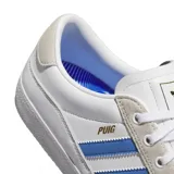 Championes adidas modelo Puig Indoor, de diseño bajo en color blanco con las icónicas tres tiras en azul claro y detalles en gamuza gris en el talón y la zona de los cordones. Presenta el nombre del modelo en dorado en el lateral.