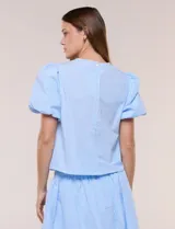 Blusa celeste a rayas blancas de calce recto con textura gofrada, cuello redondo con escote en V y mangas cortas abullonadas con elástico en los puños.