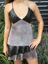 Vestido corto de tela metalizada en tono fucsia con reflejos dorados, con escote en V, diseño de top con triángulos, aberturas laterales en la cintura y doble volado irregular en el ruedo.