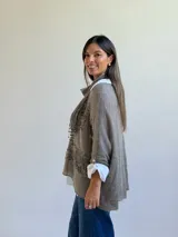 Sweater de punto color visón con diseño superpuesto, que incluye una bufanda integrada y detalles de encaje floral en el frente. Presenta mangas tres cuartos con puños abotonados y un corte holgado.