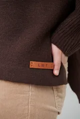 Polera de tejido de punto color chocolate, con cuello alto, mangas largas con puños acanalados y detalle de costura central vertical. Incluye una pequeña etiqueta de cuero sintético en el ruedo.