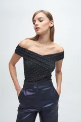 Top off-the-shoulder confeccionado en microtul negro con apliques brillantes. Presenta un diseño cruzado en el frente y ajuste al cuerpo.