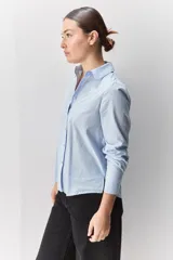 Camisa de algodón blanca, de calce relajado, con cuello clásico, mangas largas y cierre frontal con botones.