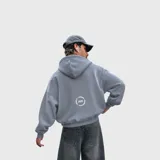 Hoodie oversize color gris, con capucha, bolsillo frontal tipo canguro y el nombre de la marca con una estrella estampados en el pecho en color blanco.