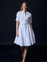 Vestido camisero blanco de algodón con cuello con solapa, delantera abotonada, mangas 3/4 regulables con presilla y botón, y cintura con lazo de ajuste.