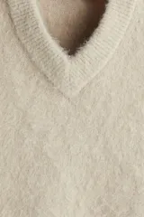 Chaleco de punto color beige claro con acabado afelpado o peludito, cuello en V y corte holgado.