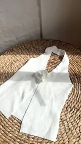 Top blanco con escote halter y detalle de flor en el centro.