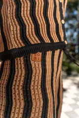 Pantalón tejido de corte recto y tiro alto, con diseño de rayas verticales onduladas en colores beige y negro. Presenta una cintura elástica con cordón ajustable.