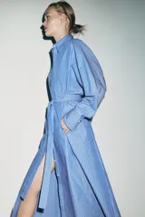 Vestido midi de corte camisero con estampado de rayas verticales, cuello solapa, manga larga con puños y cierre frontal con botones. Incluye un cinturón de lazada en el mismo tejido y bolsillos laterales ocultos.