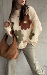 Sweater de tejido de punto color natural, con diseño de flores grandes aplicadas en tonos marrón y verde oliva. Presenta cuello redondo, mangas largas y corte holgado.