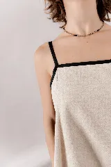 Vestido largo de lino y viscosa color beige, con escote recto, breteles finos negros y detalles de vivos negros en contraste. Presenta un calce amplio y relajado.