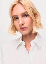 Camisa de popelín color blanco, de manga larga, con cierre frontal de botones y cuello camisero con solapa.