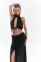 Falda larga tejida de hilo negro con destellos de lurex, tiro bajo, cintura ajustable para atar con nudo frontal y tajo pronunciado en la pierna.