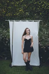 Vestido corto negro con top estilo corset, escote corazón y espalda descubierta con ajuste de cordones. La falda presenta volados superpuestos con detalle de encaje en el ruedo.