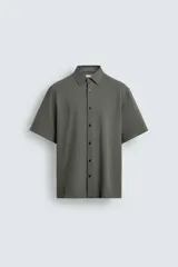 Camisa de manga corta color verde grisáceo, de corte regular fit, confeccionada en tejido suave y elástico con cierre de botonadura frontal.