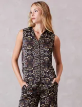 Conjunto de dos piezas compuesto por una blusa sin mangas con cuello solapa y escote en V con botones frontales, y un pantalón de tiro alto con pierna ancha y bolsillos laterales. Ambas prendas están confeccionadas en satén con un estampado floral sobre fondo oscuro.