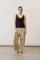 Cartera de mano de macramé color crudo con apliques de caracoles y flecos colgantes en la parte inferior. Cuenta con asas rígidas integradas en el mismo tejido.