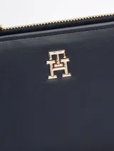 Billetera plegable Tommy Hilfiger color azul marino, de acabado granulado, con cierre de botón a presión, múltiples ranuras para tarjetas, compartimento para billetes y bolsillo exterior con cremallera. Presenta el monograma TH metálico en la parte delantera.