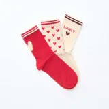 Set de tres pares de calcetines de caña media. Un par es de color rojo con un corazón blanco, otro par es de color crema con corazones rojos y el tercer par es de color crema con la palabra "Lovely" y un corazón marrón.
