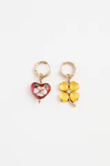 Par de aros tipo argolla con dijes colgantes asimétricos: uno con forma de corazón esmaltado en rojo con diseño floral y otro con forma de trébol de cuatro hojas en acrílico amarillo con un cristal central.
