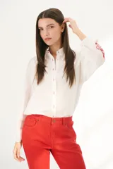 Camisa color crema con bordados florales marrones en las mangas, corte clásico, cuello camisero y cierre frontal con botones.