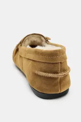 Mocasín de mujer confeccionado en serraje color tostado, con detalle de fruncido y borlas en la parte delantera. Presenta un interior forrado en tejido efecto borreguito y suela plana.