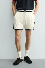 Short deportivo de tejido de punto con estructura abierta, color blanco con vivos a contraste en azul marino. Presenta cintura elástica, bolsillos frontales, aberturas laterales en el bajo y etiquetas conmemorativas de la Copa Mundial de la FIFA Francia 98.